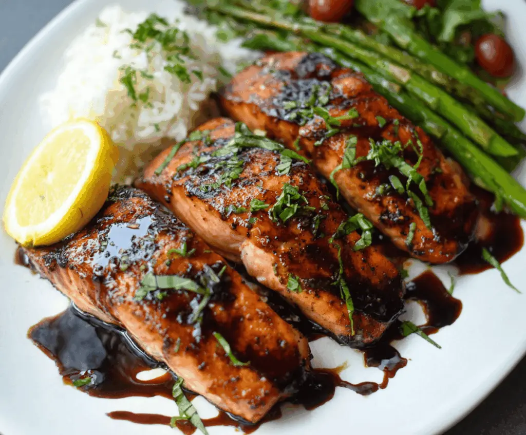 Delicious balsamic glazed salmon fillet garnished with fresh herbs on a white plate.