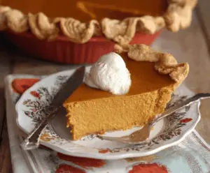 Creamy Pumpkin Butter Pie topped with whipped cream and a cinnamon spice garnish on a rustic pie plate.