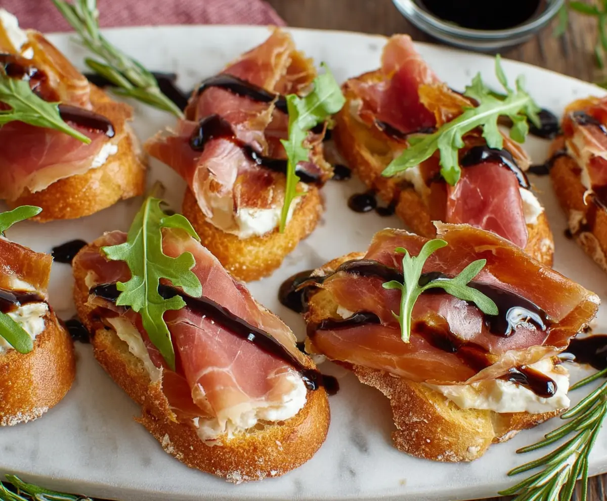 Crispy crostini topped with melted Brie cheese and thin slices of prosciutto, served on a rustic wooden platter.