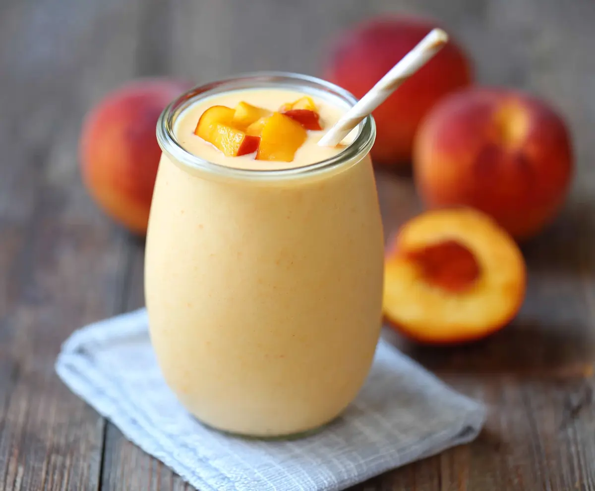 Healthy Peach Protein Smoothie in a glass with fresh peaches and almonds on a white background.