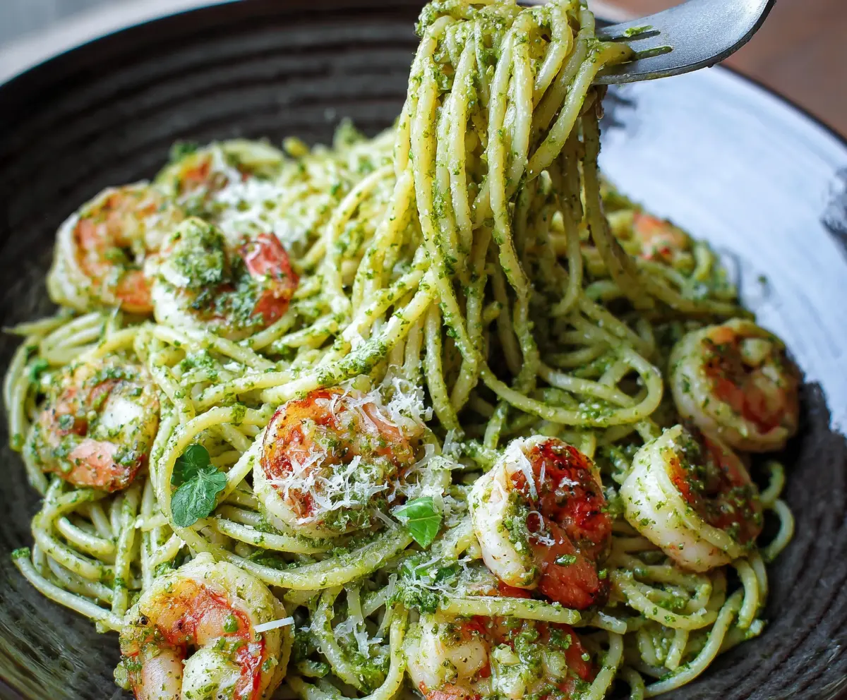 Delicious pesto shrimp pasta with fresh basil and melted cheese on a white plate