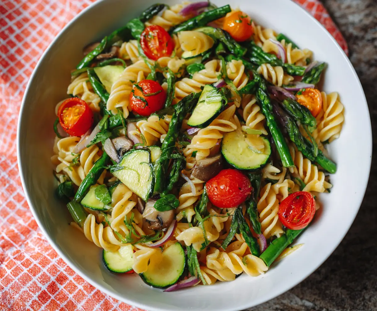 Colorful Pasta Primavera with fresh vegetables and herbs on a white plate.